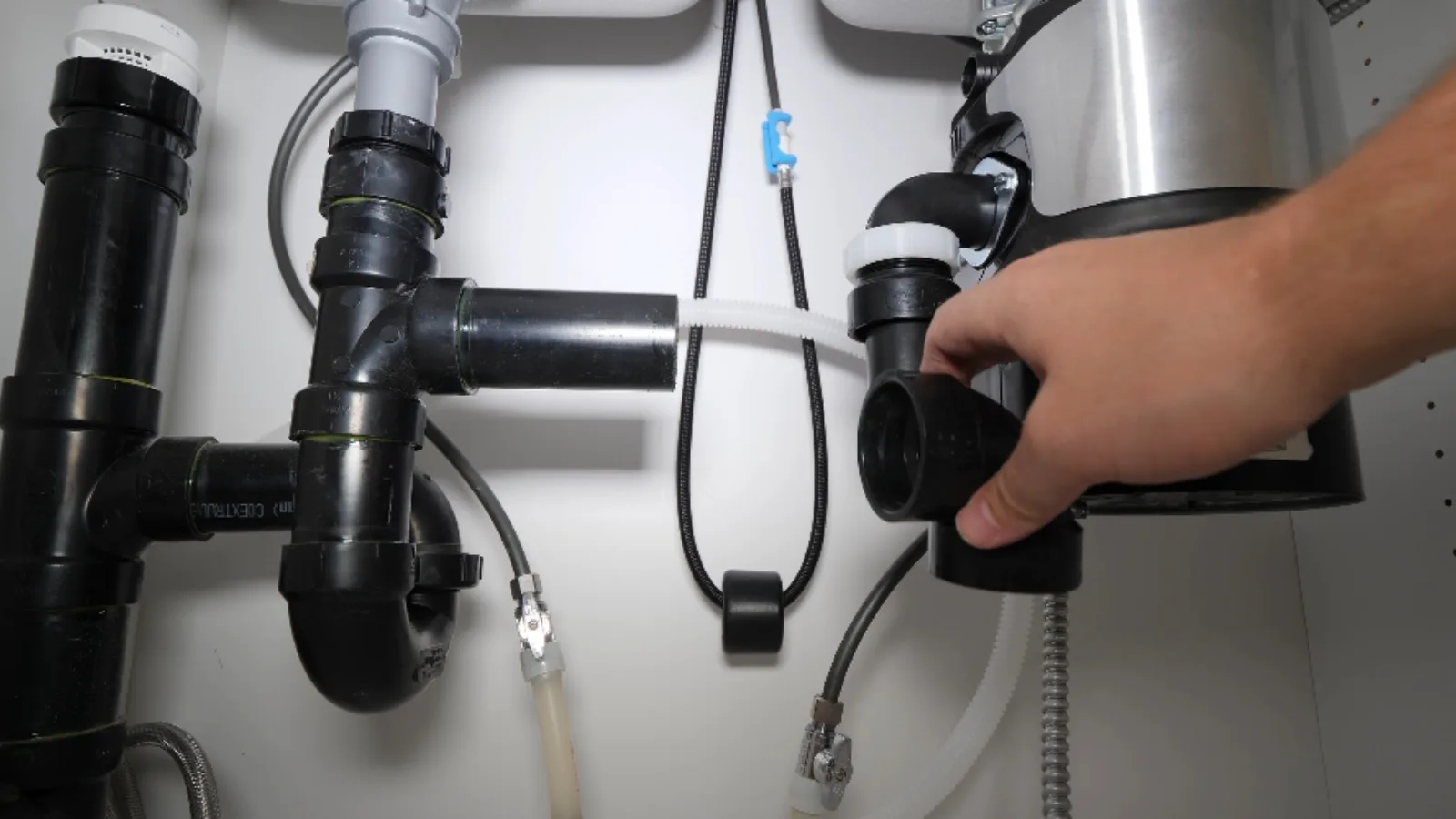 Hand adjusting a garbage disposal and drain connections under a sink