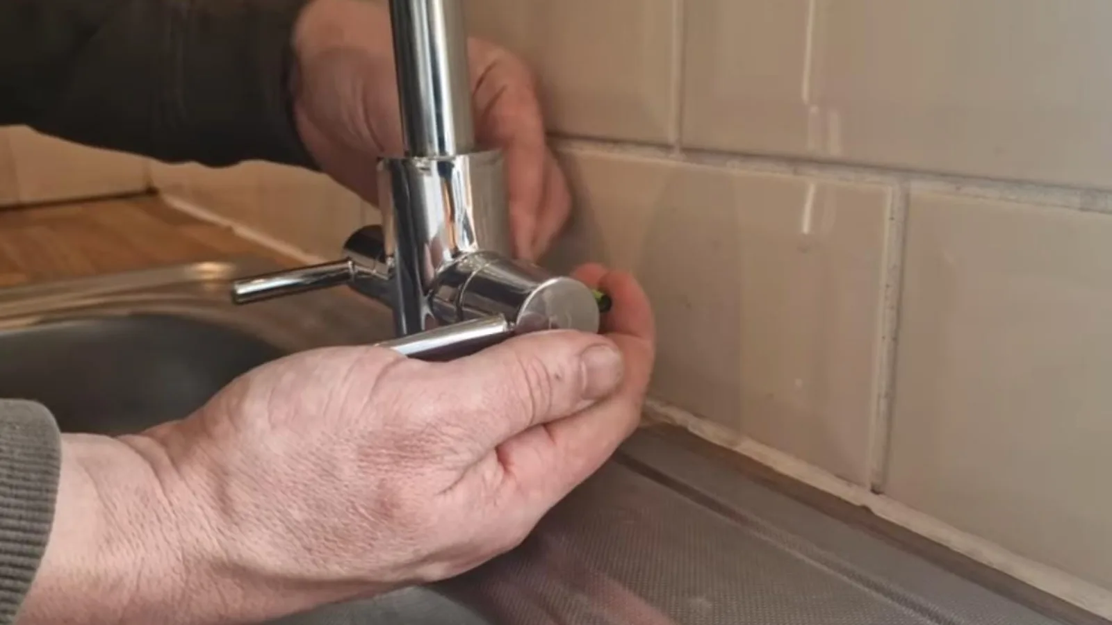 Hands working on a kitchen faucet at the sink
